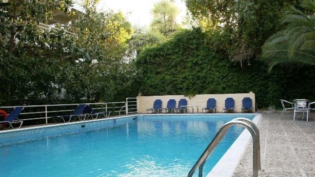 A swimming pool with blue water, surrounded by a tiled deck and a fence. - Stefanakis Hotel & Apartaments (Vari-Voula-Vouliagmeni)