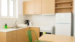 A compact kitchen with wooden cabinets, a white countertop, a sink, a stove, and a refrigerator. - Stefanakis Hotel & Apartaments (Vari-Voula-Vouliagmeni)