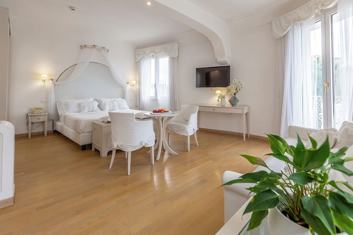 A hotel room with a bed, a desk, a TV, and a dining area.