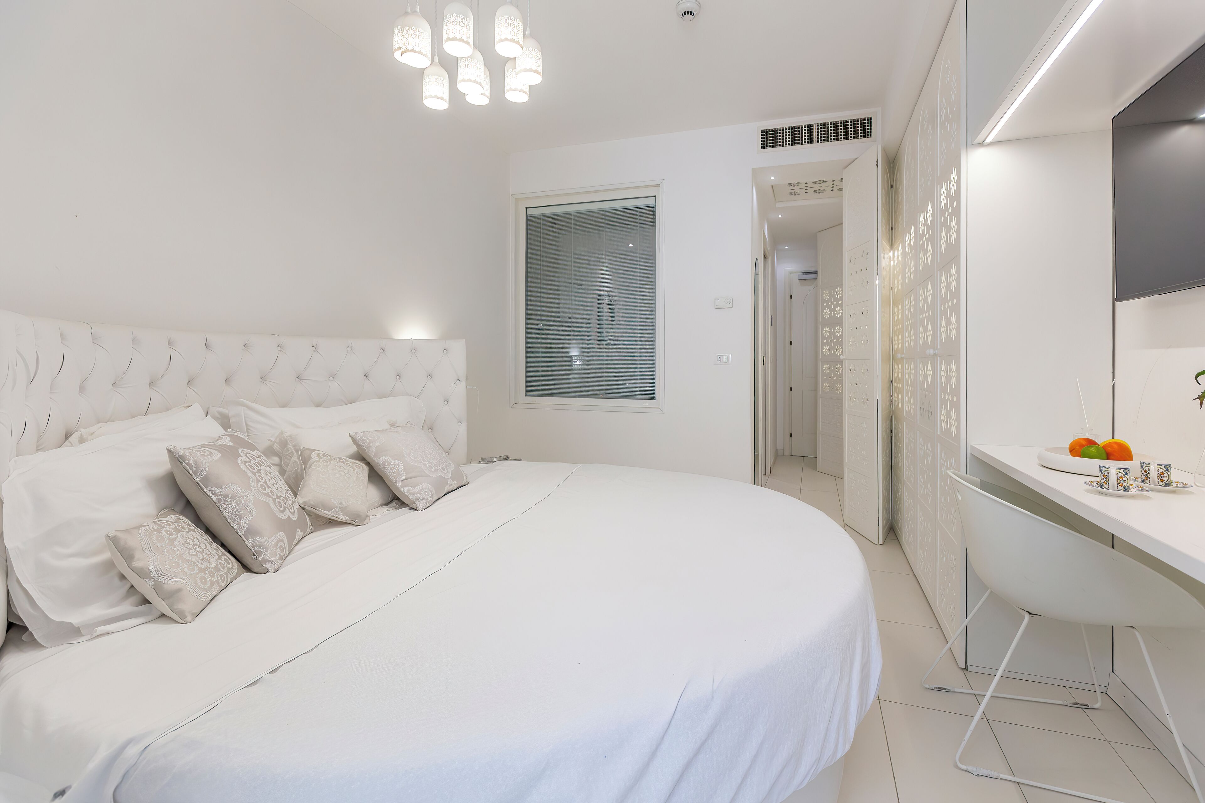 A modern bedroom with a large bed, a bedside table with fruit, and a view of a hallway.