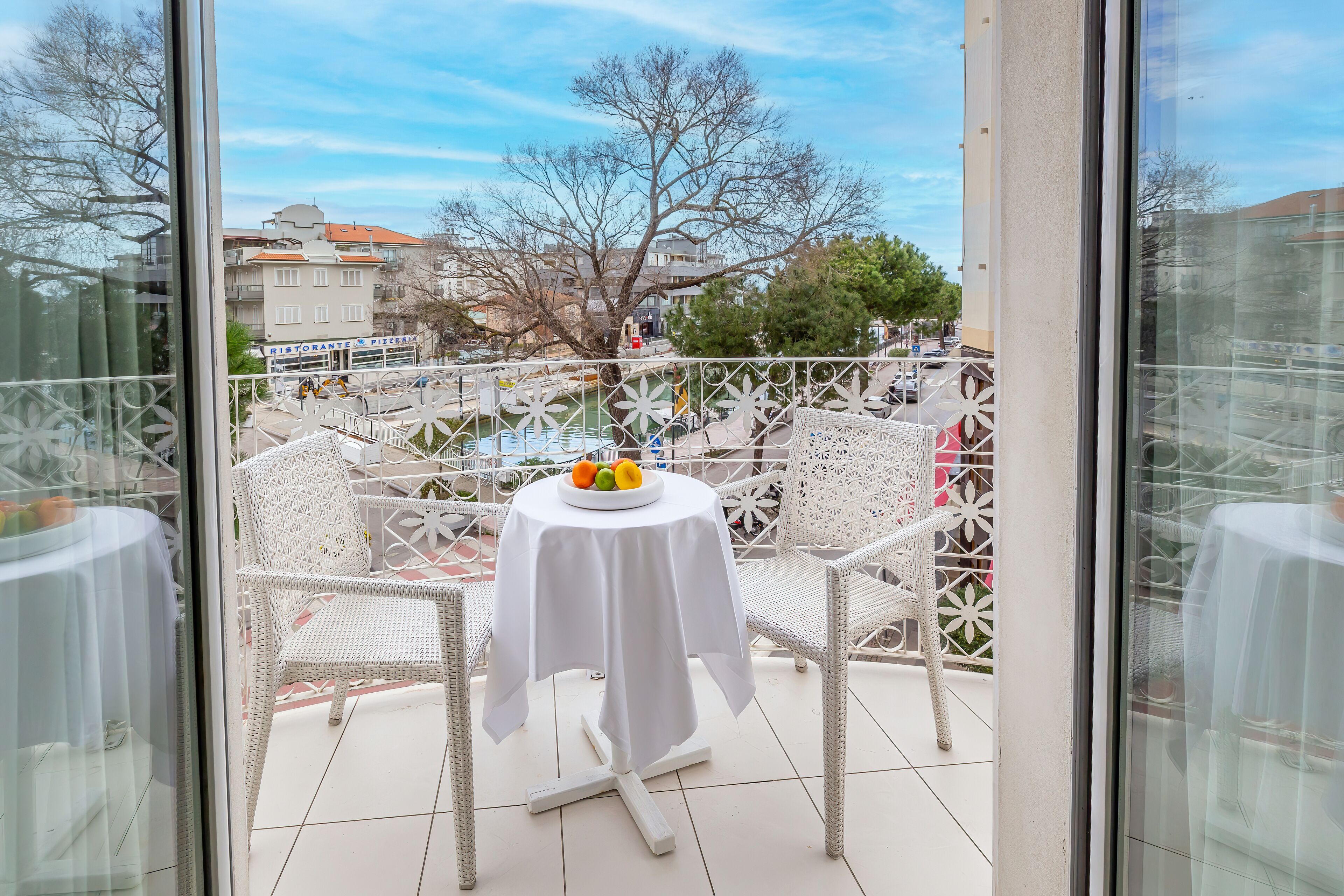 A balcony with a table and chairs, a fruit bowl, and a view of buildings and trees.