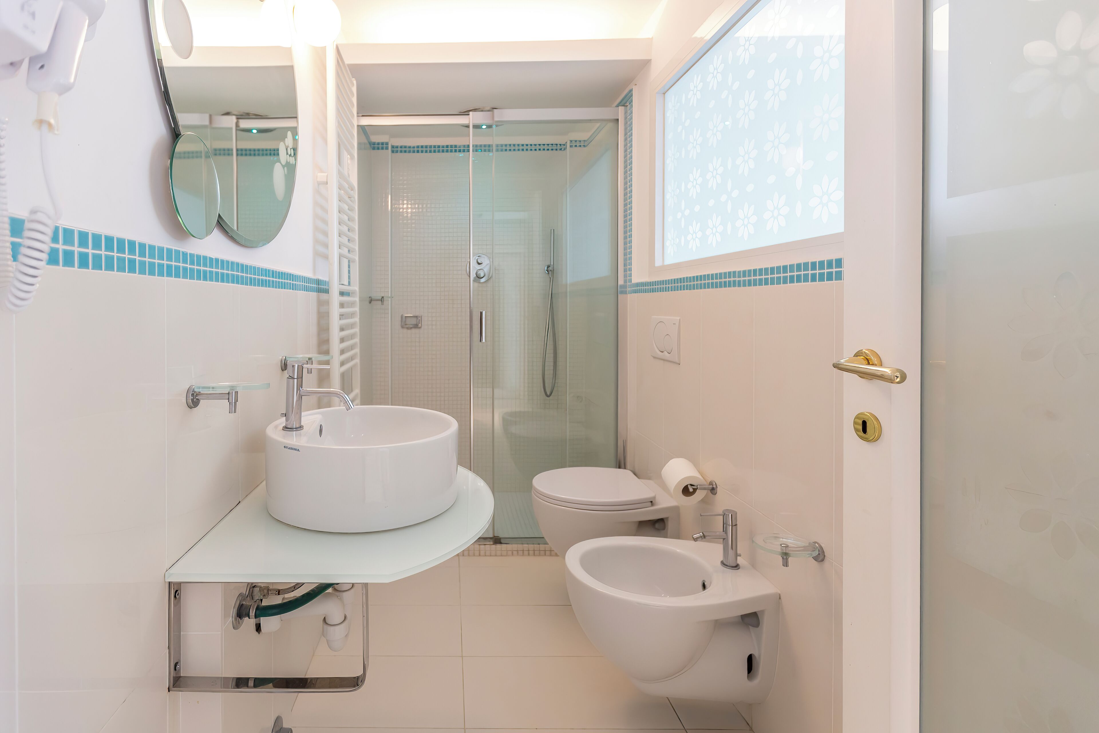 Un baño moderno con ducha de mampara de vidrio, lavamanos blanco y un bidé.