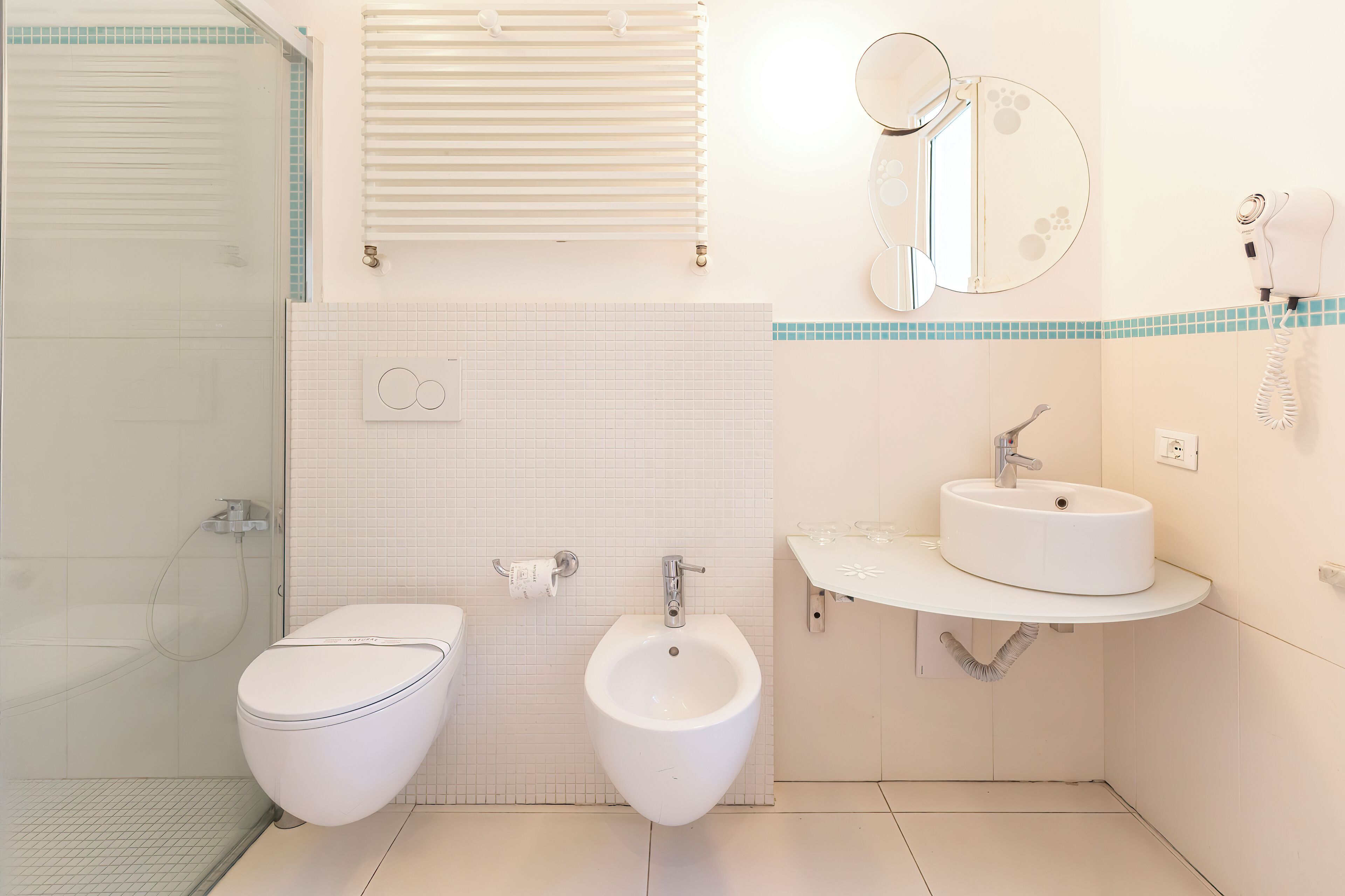 Une salle de bain moderne équipée d’un bidet, d’un lavabo, d’un miroir et d’un porte-serviettes.