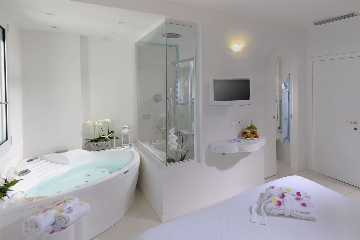 A modern bathroom with a bathtub, a shower, a vanity with a mirror, and a television mounted on the wall.
