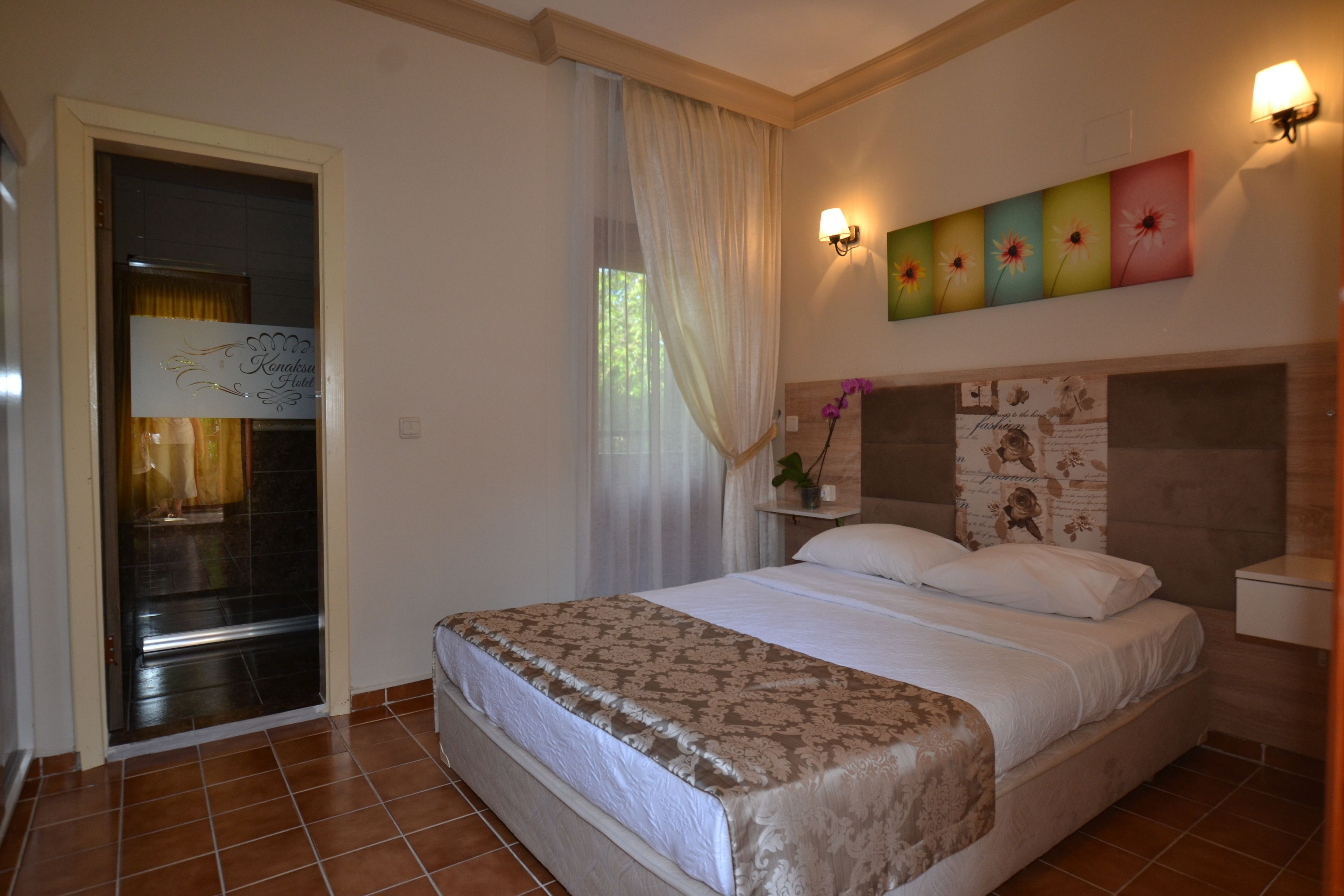 Una habitación de hotel con una cama, una mesita de noche, una lámpara de pared, una ventana con cortinas y una puerta con un letrero.