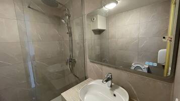 A modern bathroom with a glass-enclosed shower, a white sink, and a mirror reflecting a hand dryer and soap dispenser.