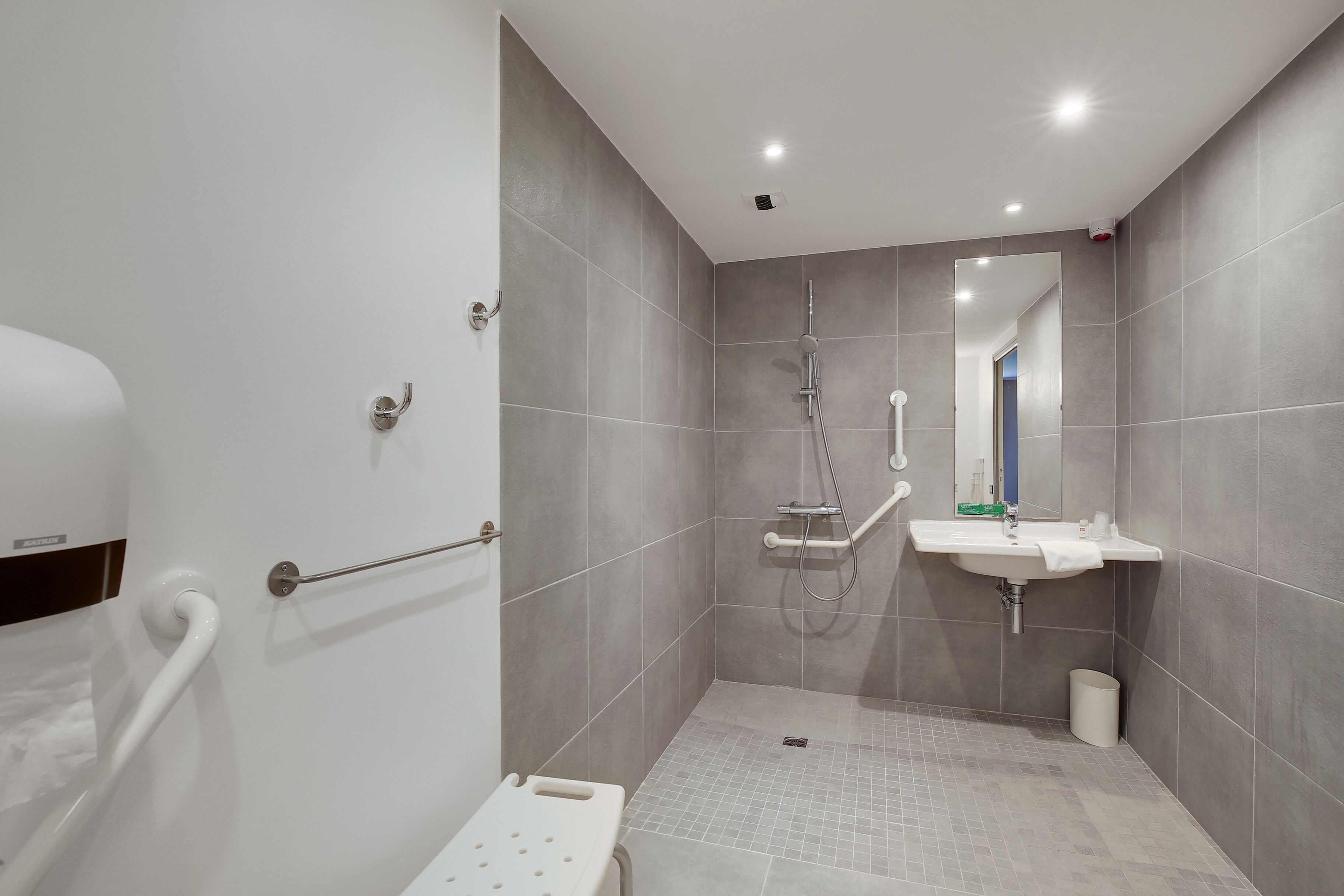 A modern bathroom with a walk-in shower, grab bar, and a sink with a mirror.