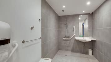 A modern bathroom with a walk-in shower, grab bar, and a sink with a mirror.