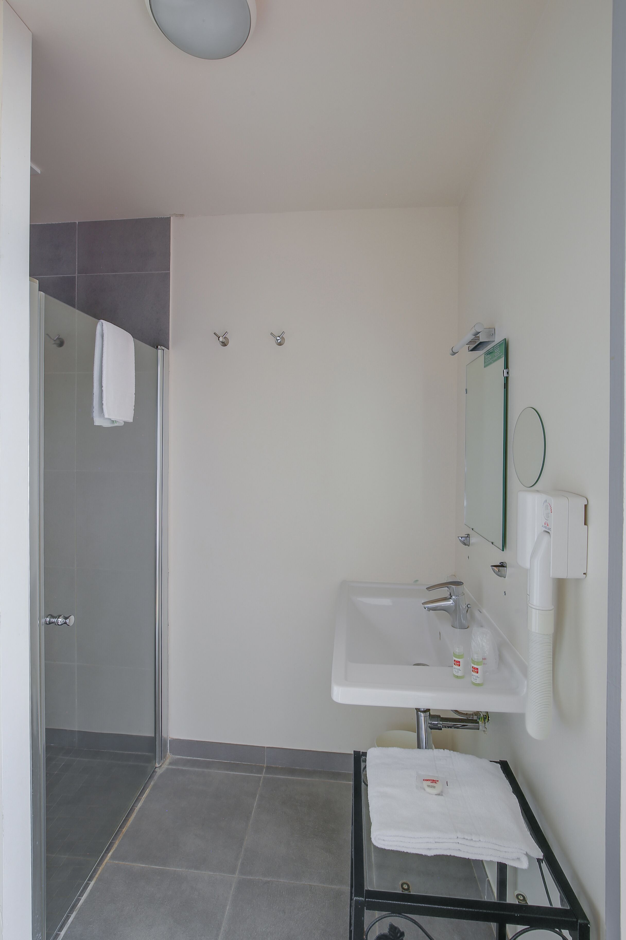 A bathroom with a glass shower enclosure, a white sink with a mirror, and a towel rack.