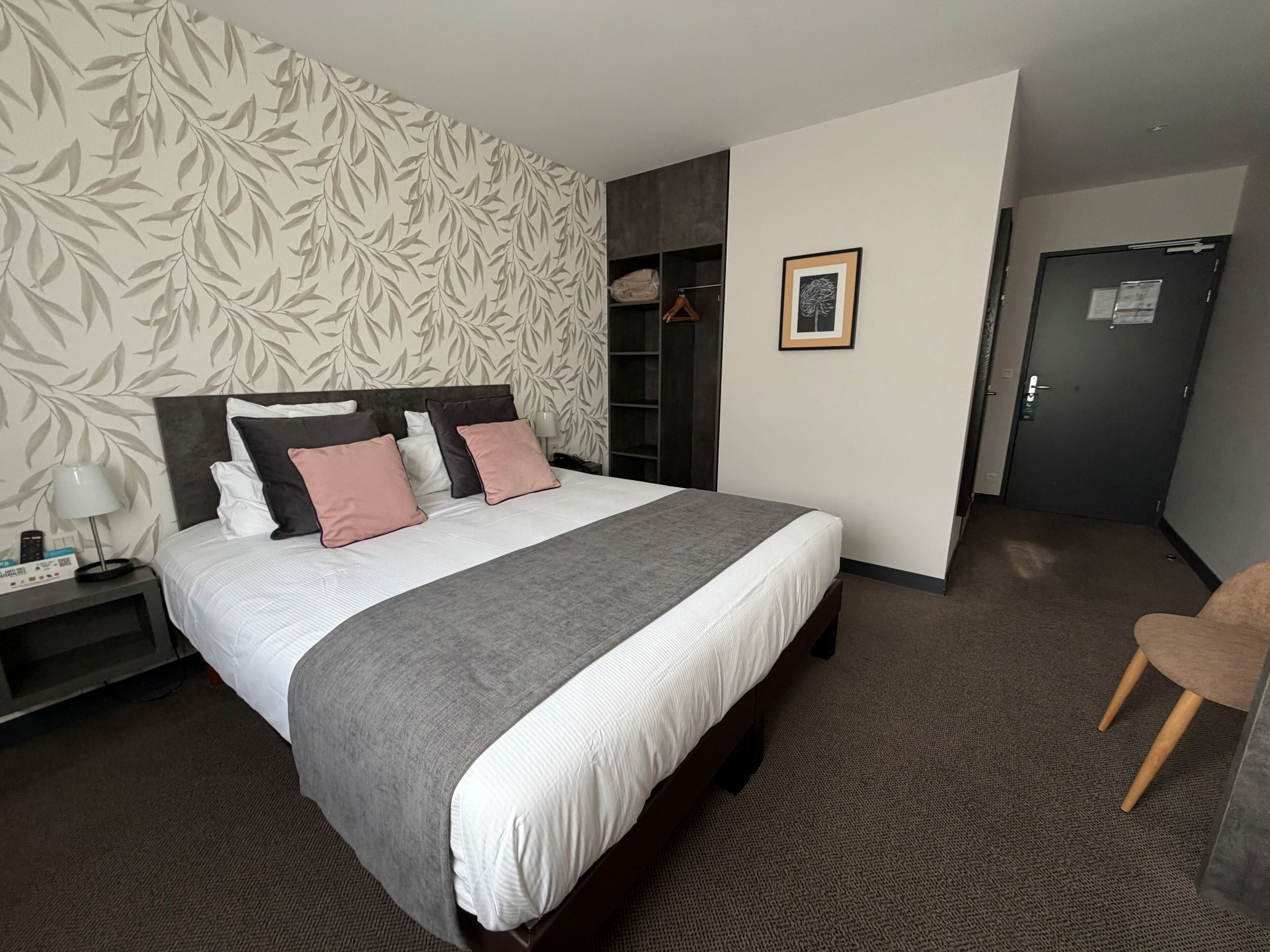 Une chambre d’hôtel avec un grand lit, une armoire, une table de chevet avec une lampe et un tableau encadré au mur.