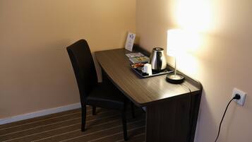 A hotel room with a wooden desk, a chair, a lamp, a kettle, and a tray with a cup and a menu.