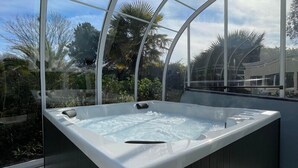 A hot tub with a glass enclosure, surrounded by greenery and a clear sky. - Hotel Arcadia (Lannion)