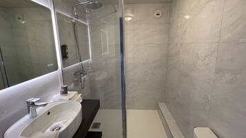 A modern bathroom with a glass-enclosed shower, a white sink, and a large mirror.