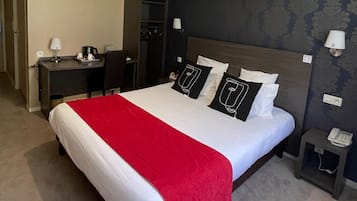 A hotel room with a large bed, a desk, a chair, a wardrobe, and a nightstand with a phone.