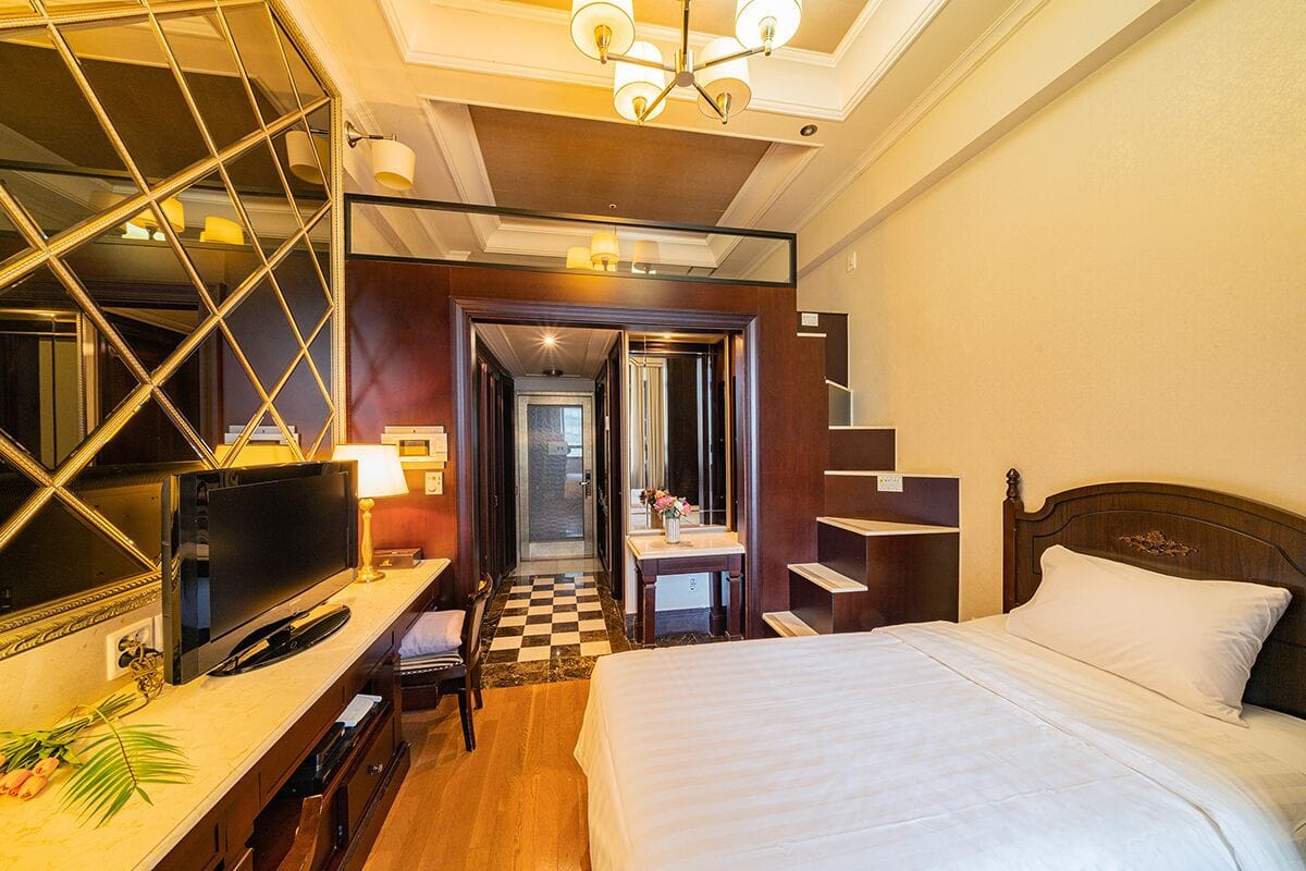 Quarto de hotel com cama, televisão, escrivaninha com luminária e espelho.