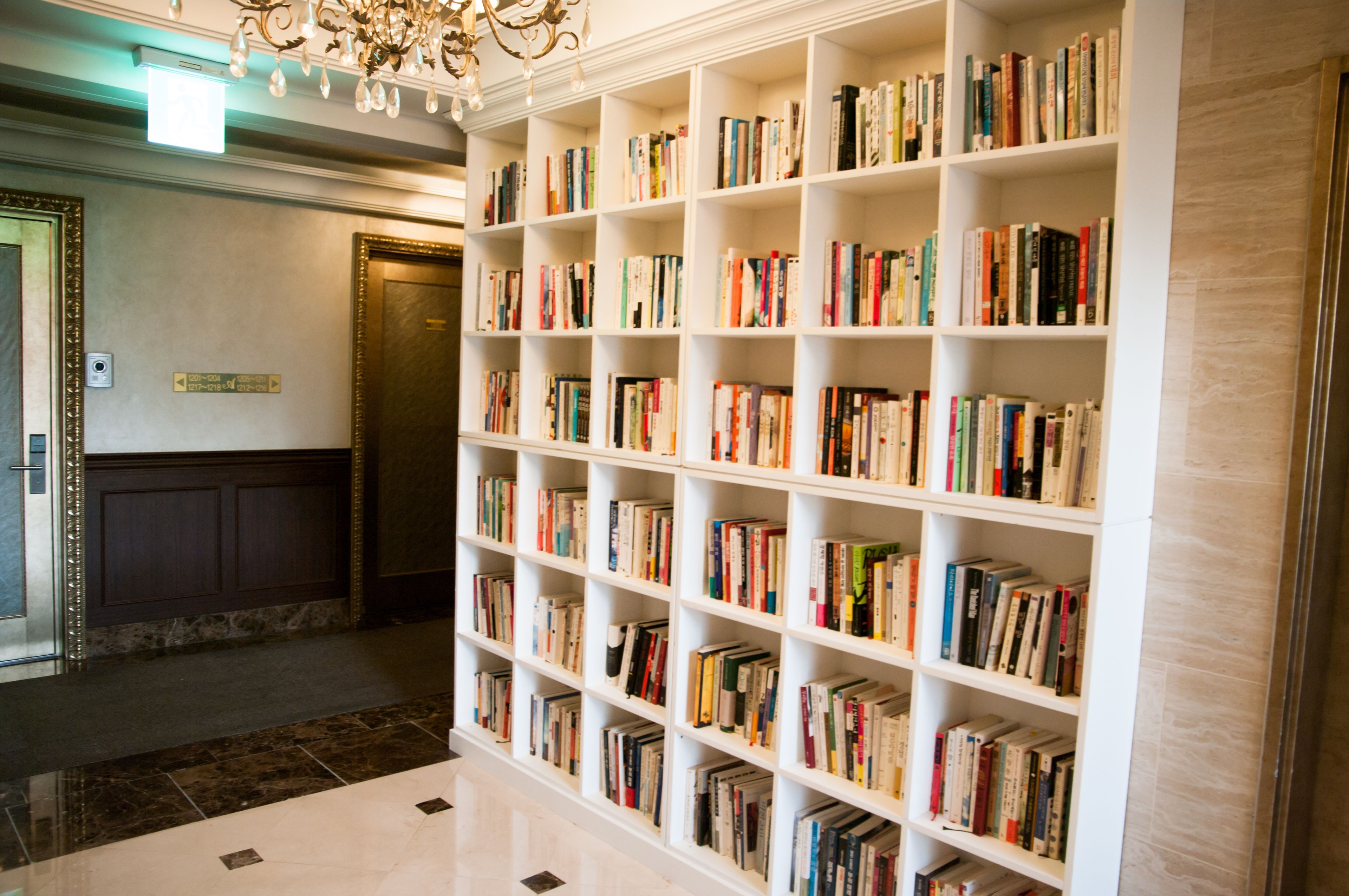 A library with white shelves filled with books, a chandelier, and a marble floor.