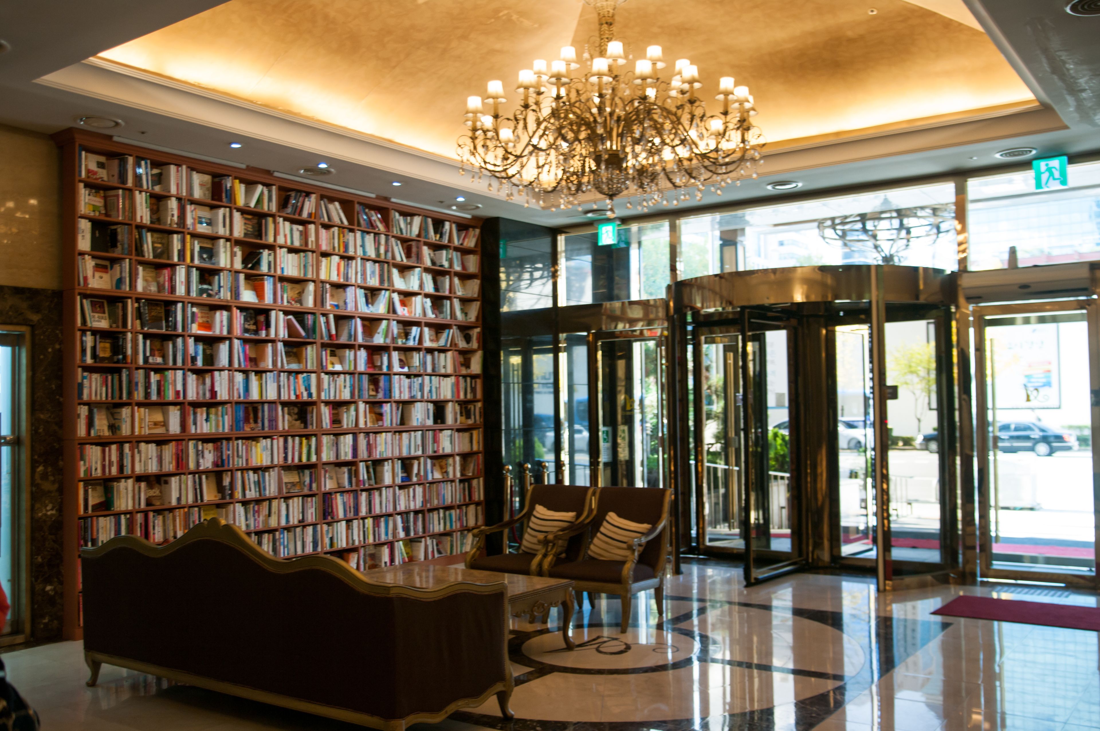 A lobby with a large bookshelf, a chandelier, a revolving door, and a seating area.
