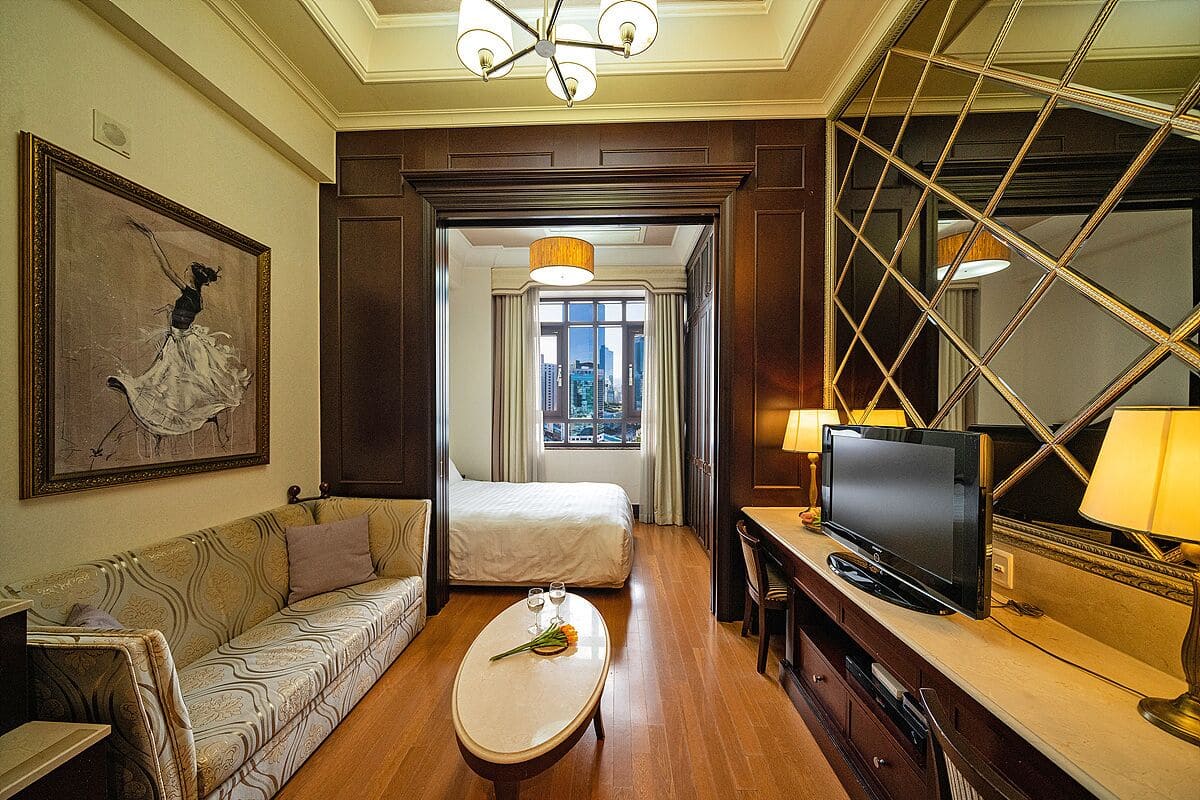 Quarto de hotel com cama, sofá, televisão e mesa de jantar com um vaso de flores.
