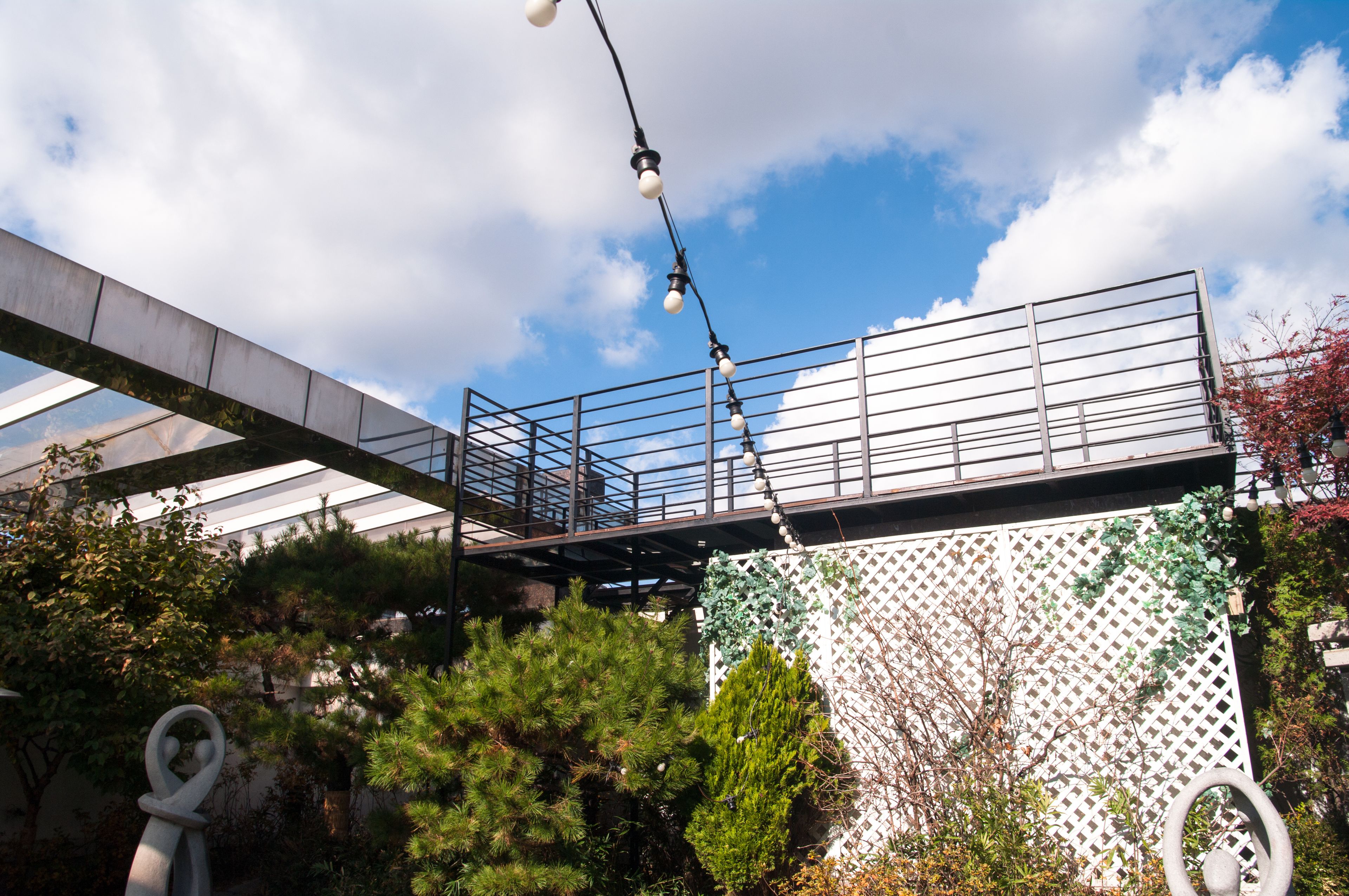 Eine Brücke mit Metallgeländern, einem weißen Gitterzaun und verschiedenen Pflanzen.