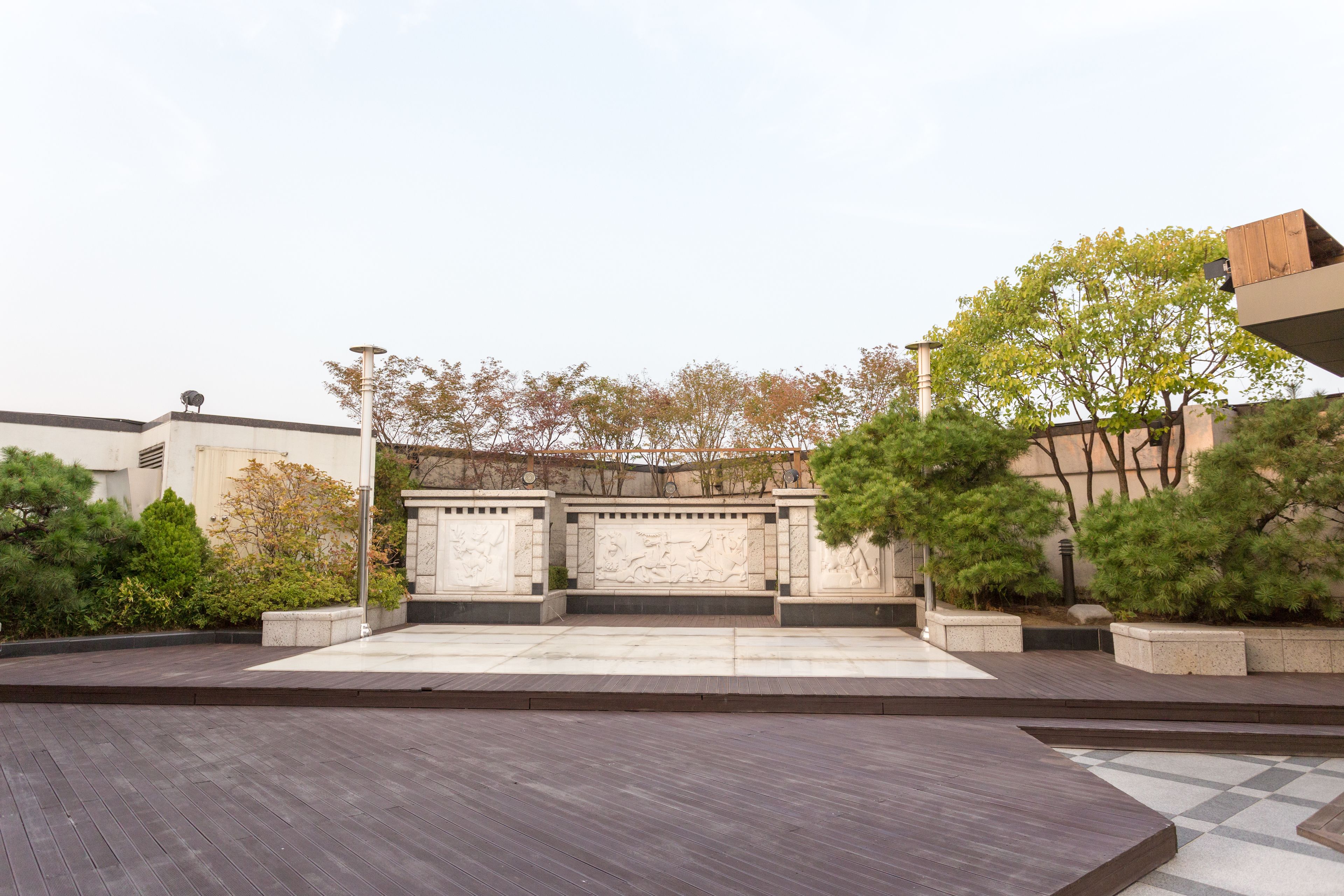 A courtyard with a wooden deck, stone benches, and a stone wall with carvings.
