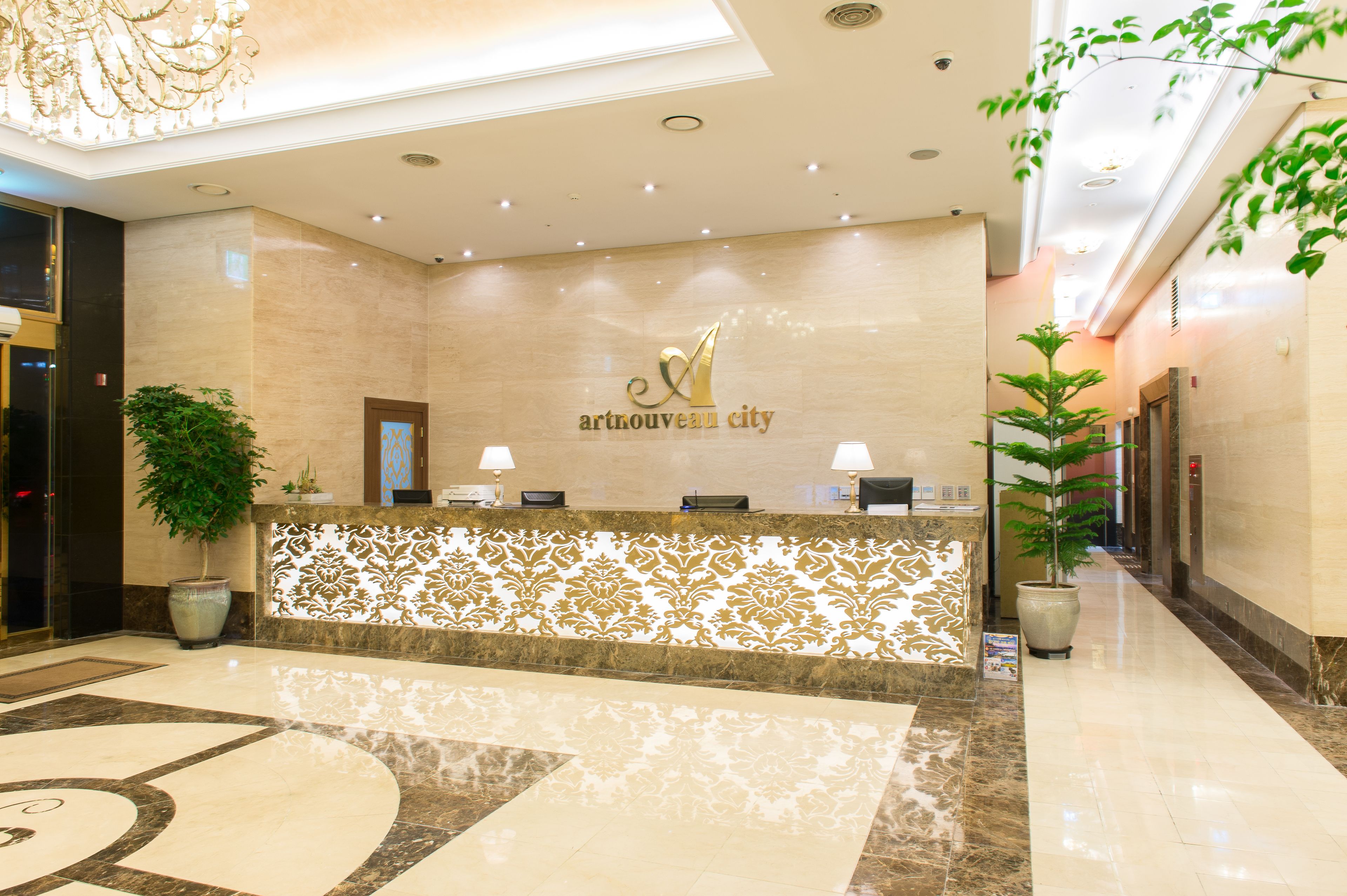 A reception area with a marble floor, a reception desk, two lamps, and a large potted plant.