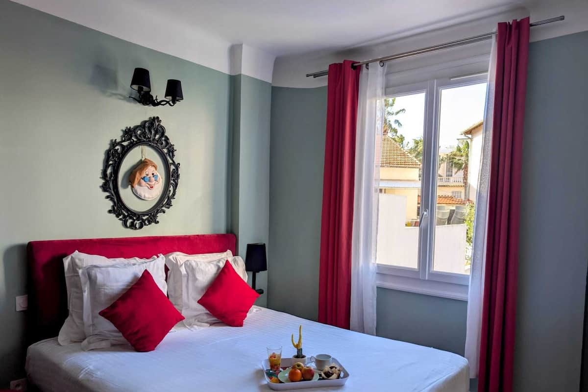 A neatly made bed with red and white pillows, a tray of breakfast items, and a framed picture on the wall.