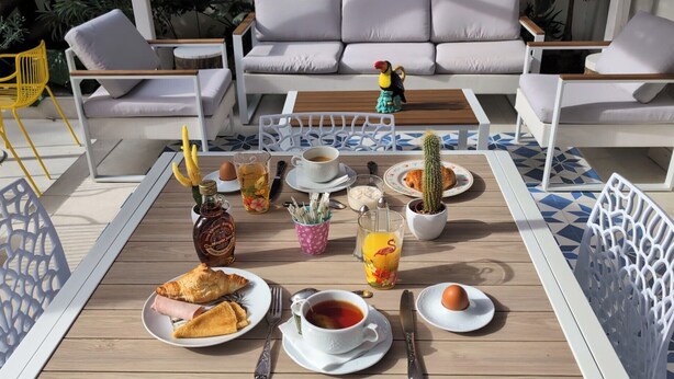 Une table en bois dressée pour le petit-déjeuner, avec une variété d’aliments, de boissons et un cactus.