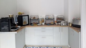 Une petite cuisine équipée d’un four à micro-ondes, d’un grille-pain et d’une machine à café. On y trouve deux meubles de rangement aux portes en verre, contenant des aliments et des condiments.