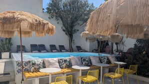 Un espace aménagé au bord de la piscine, comprenant une piscine, des chaises longues, des chaises jaunes et des parasols en chaume.