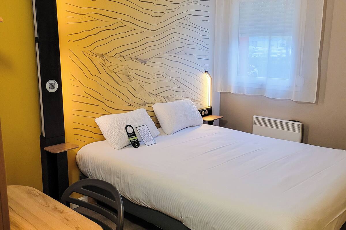 A hotel room with a bed, bedside table, chair, and a wall with a unique design.