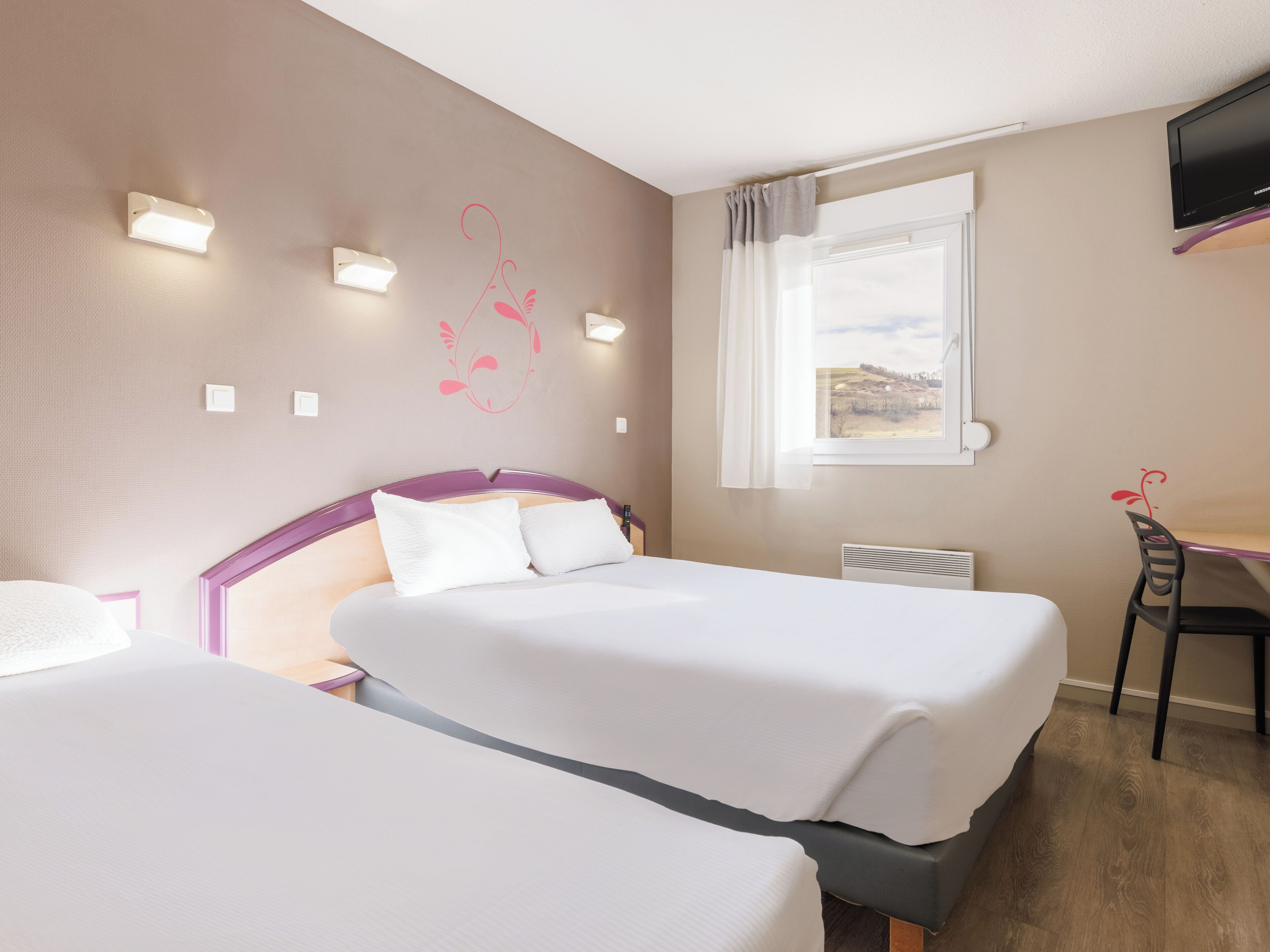Une chambre d’hôtel avec deux lits, un bureau, une chaise, une télévision et une fenêtre donnant sur un beau paysage.