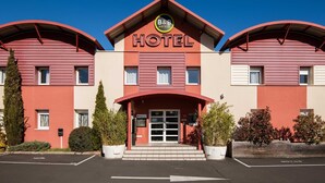 A B&B hotel with a red and beige facade, a central entrance with a glass door, and a parking lot in front.