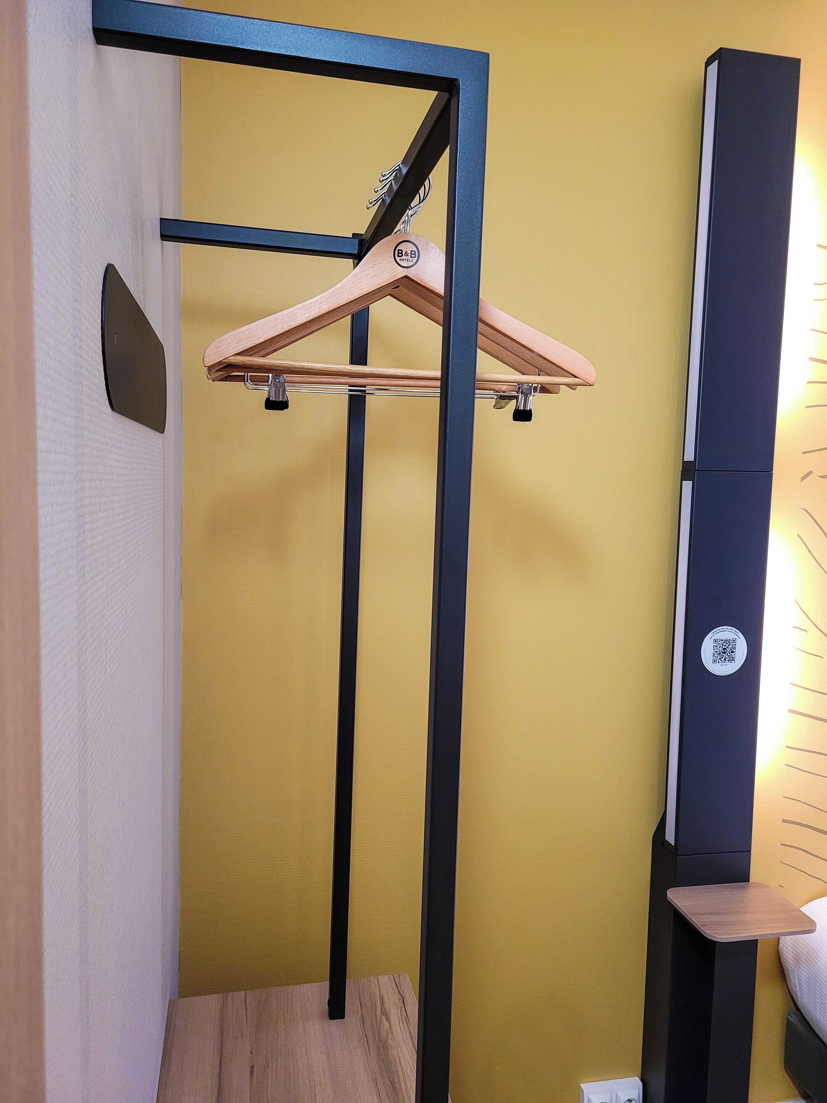 Ein Raum mit einem hölzernen Kleiderbügel an einem schwarzen Metallgestell, einer schwarzen vertikalen Stange und einem kleinen Holztisch.