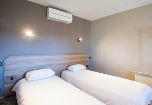 A hotel room with two beds, a wooden headboard, an air conditioning unit, and a wall-mounted light fixture.