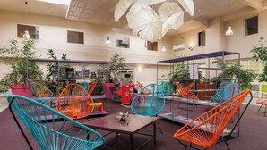 A spacious indoor area with colorful chairs, tables, and potted plants.