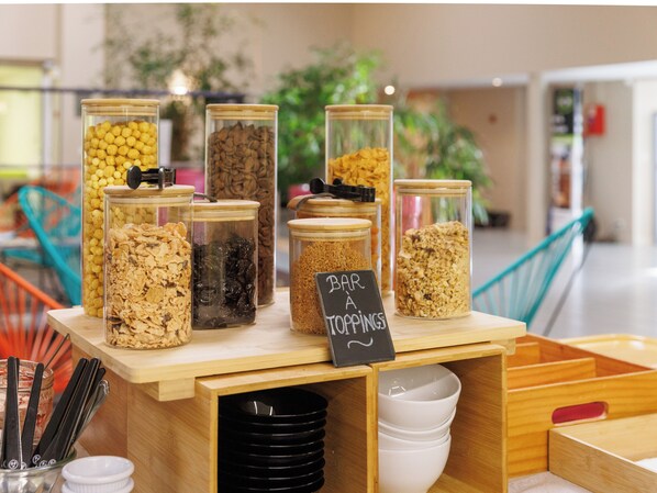 Una estación de autoservicio con diversos alimentos en frascos de vidrio, un cartel que indica 'BAR A TOPPINGS' y un cartel que dice 'BAR A'.
