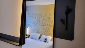 A hotel room with a bed, a bedside table, and a mirror reflecting the room.