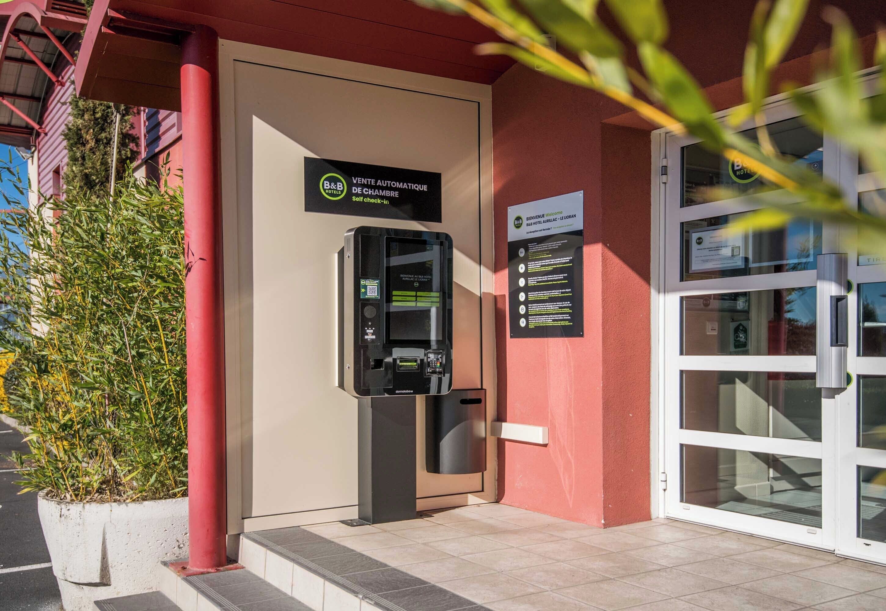 Un kiosque en libre-service, une porte avec une pancarte et une plante en pot devant un bâtiment.