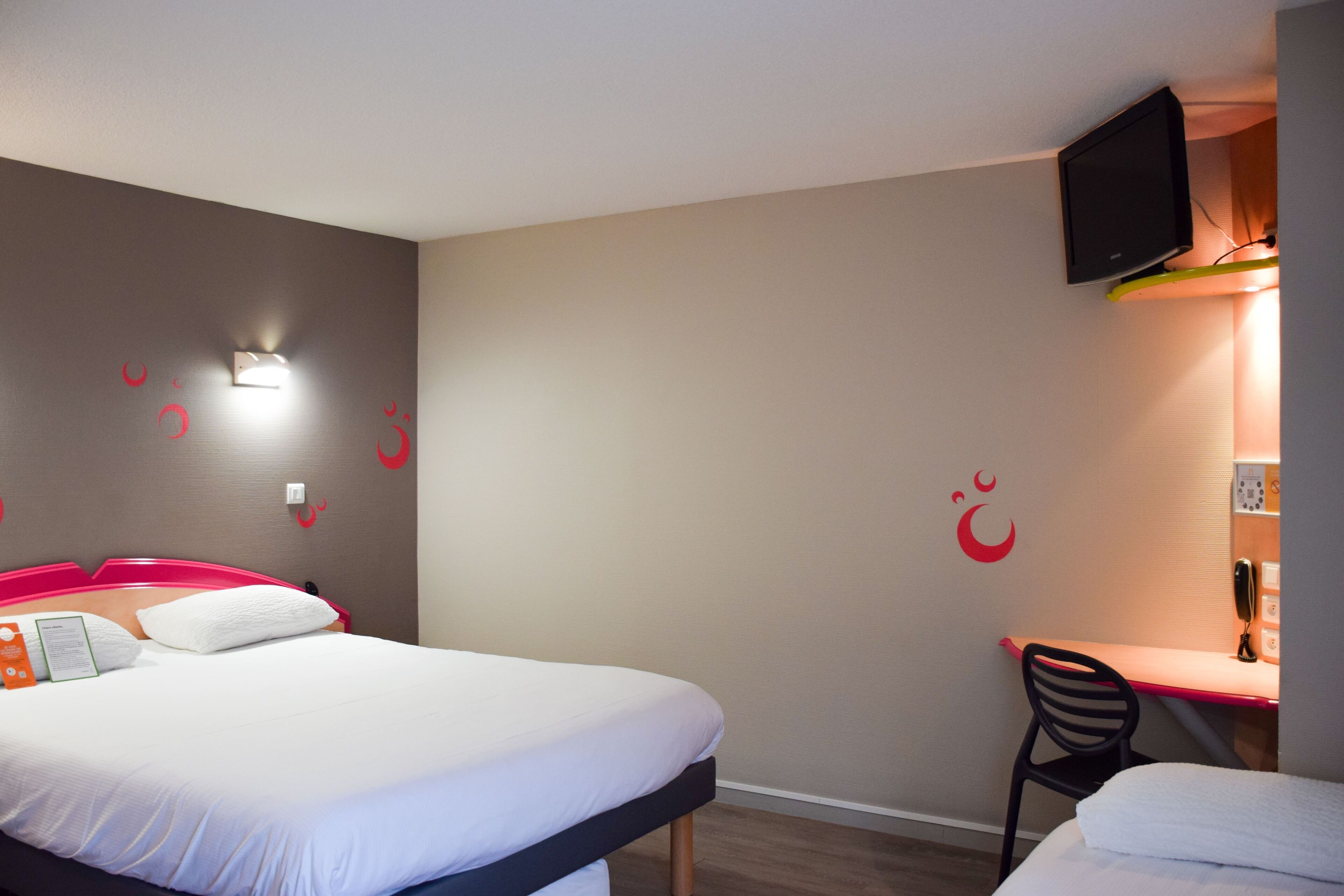 A hotel room with a bed, a desk, and a TV mounted on the wall.