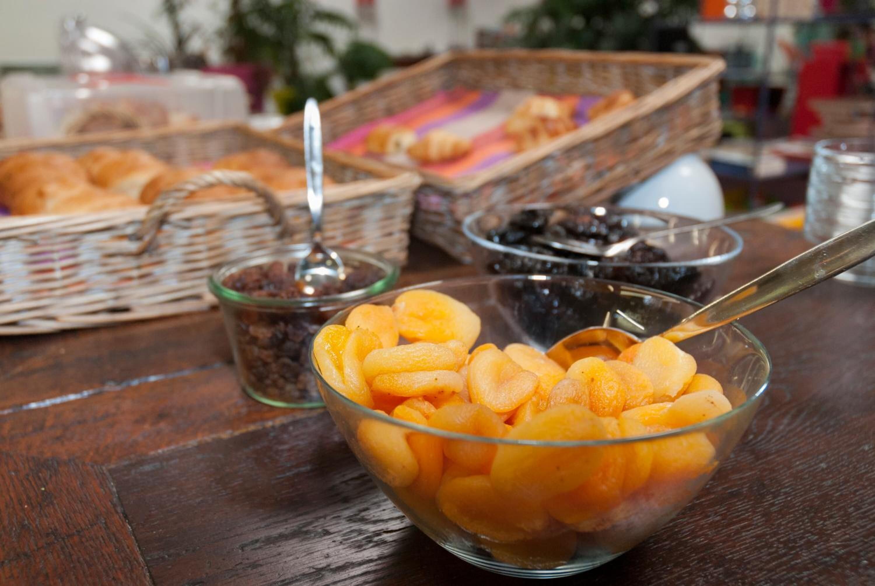 A table with a glass bowl of sliced fruit, a basket of bread, and a glass of juice.