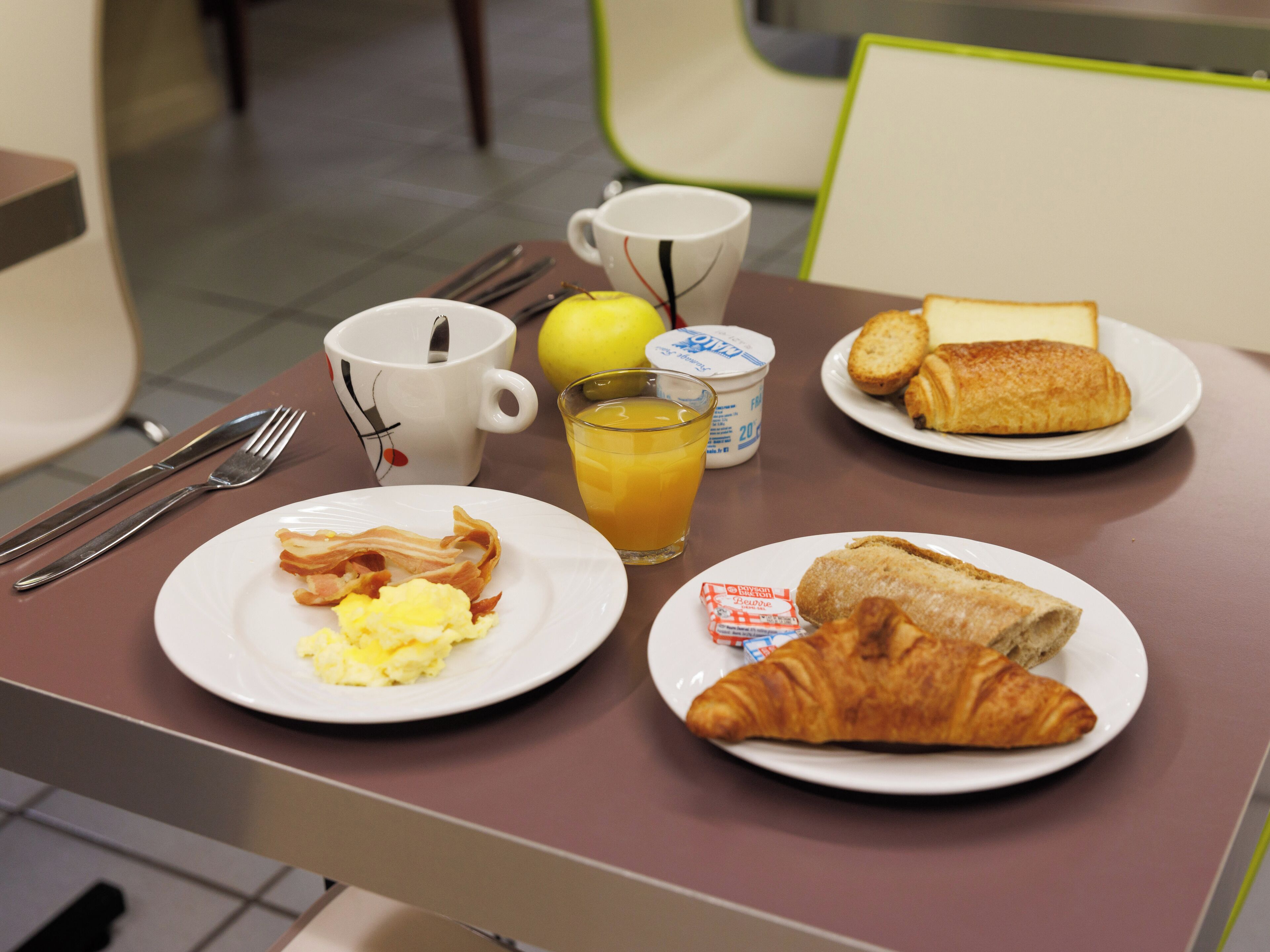 A breakfast table with plates of food, a cup, and a glass of orange juice.