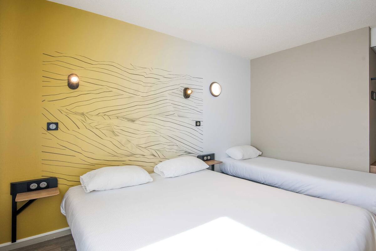 A hotel room with two beds, a wall with a textured design, and a nightstand with a power outlet.