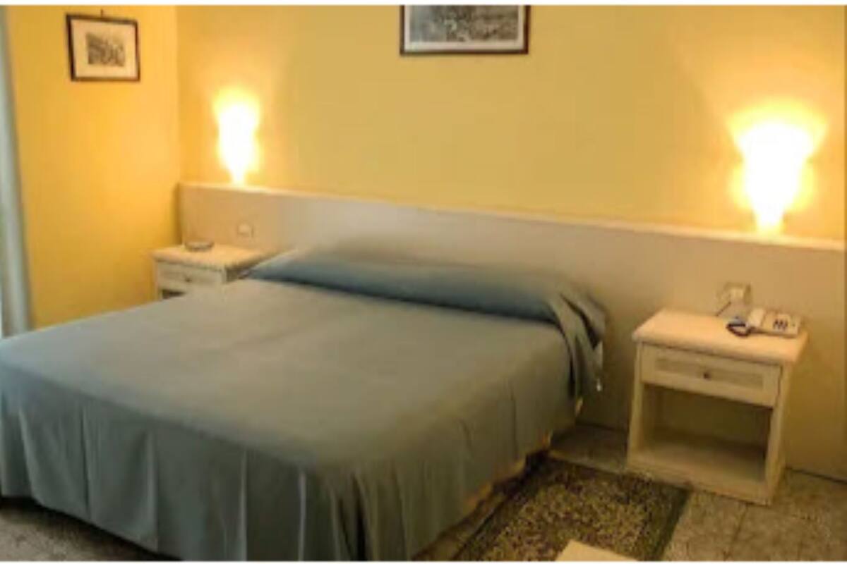 A standard hotel room with a single bed, bedside tables, and wall-mounted lamps.