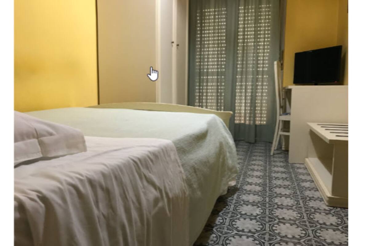 A hotel room with a bed, a television on a stand, a wardrobe, and a patterned floor.