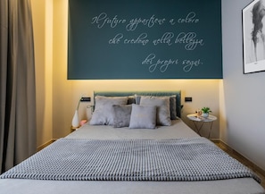 A bedroom with a bed, pillows, a bedside table, and a wall with a quote. - Hotel Europa (Pontecagnano Faiano)