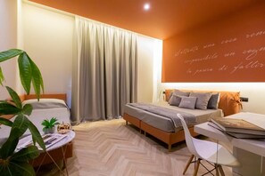 A modern bedroom with a bed, a desk, and a chair. There is a window with curtains, a plant, and a wall with a quote. - Hotel Europa (Pontecagnano Faiano)