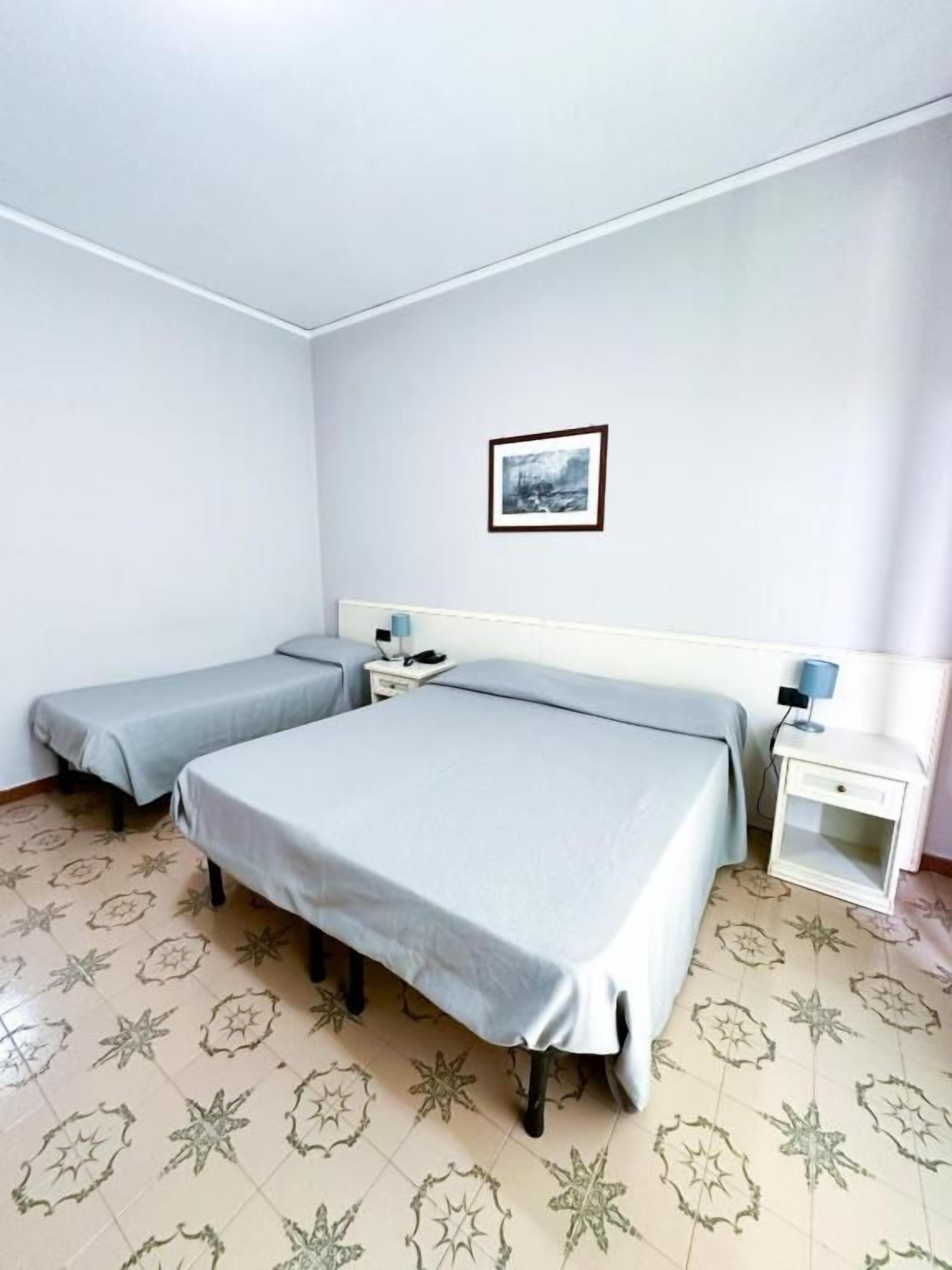 A room with two beds, a nightstand, a small table, and a framed picture on the wall.