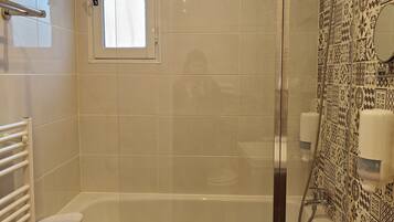 Een badkamer met een bad, een douche en een raam.