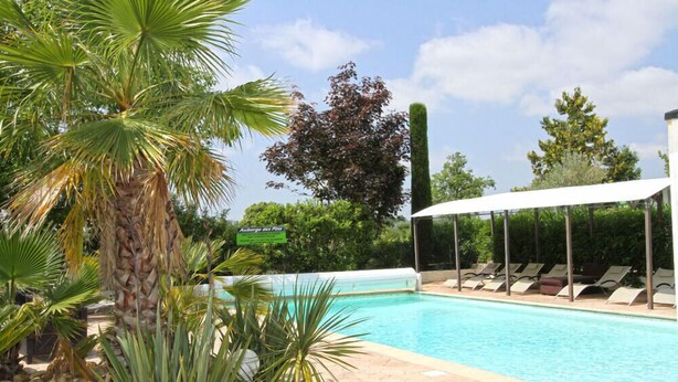 Una piscina con sillas de descanso y una zona techada, rodeada de palmeras y un letrero que dice "Auberge des Pins".