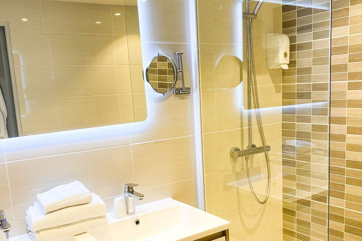 A modern bathroom with a glass shower enclosure, a sink with a mirror, and neatly folded towels.